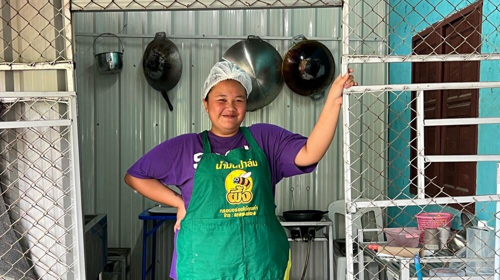 Una mujer con un delantal verde se encuentra en una cocina donde se prepara Dok Jok.