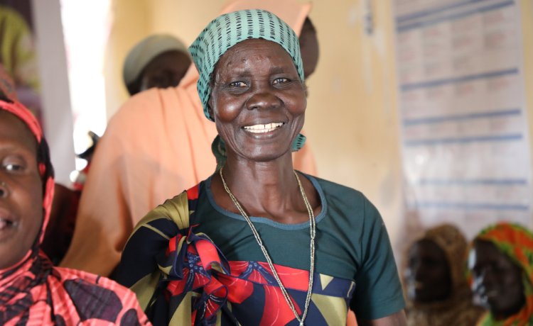 A woman in a pale green headscarf and dark green t-shirt smiles into the camera