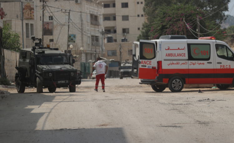  A Palestinian Red Cross Society paramedic stands on the road in front of an Israeli army jeep.